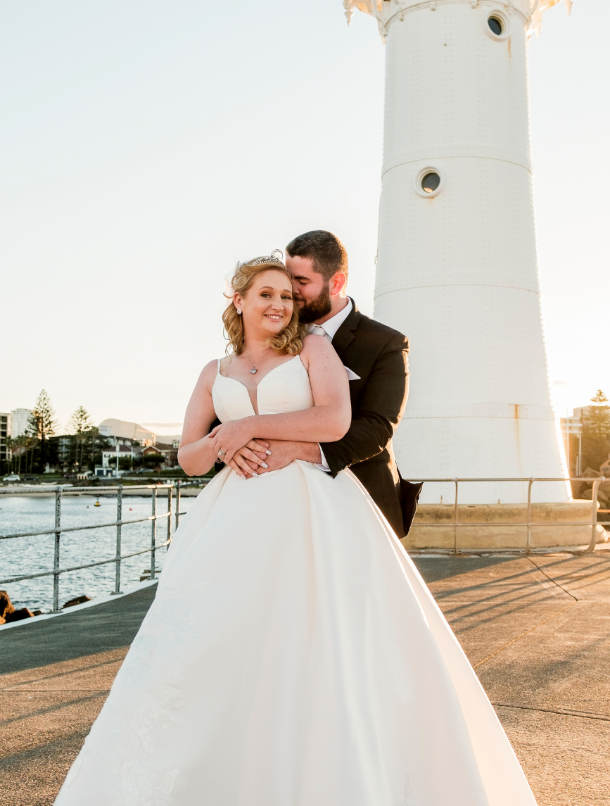 Bride and groom posing for wedding photographer at Wollongong Breakwater Lighthouse