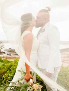 1 bride and groom kissing under veil on beach