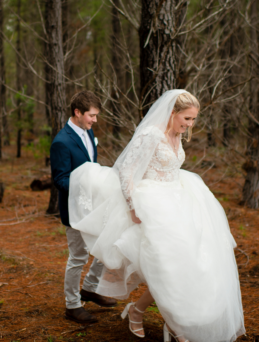 groom holding brides dress while walking through forest in winter