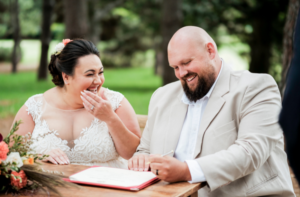 1 bride and groom laughing while signing marriage certificate at Sydney wedding