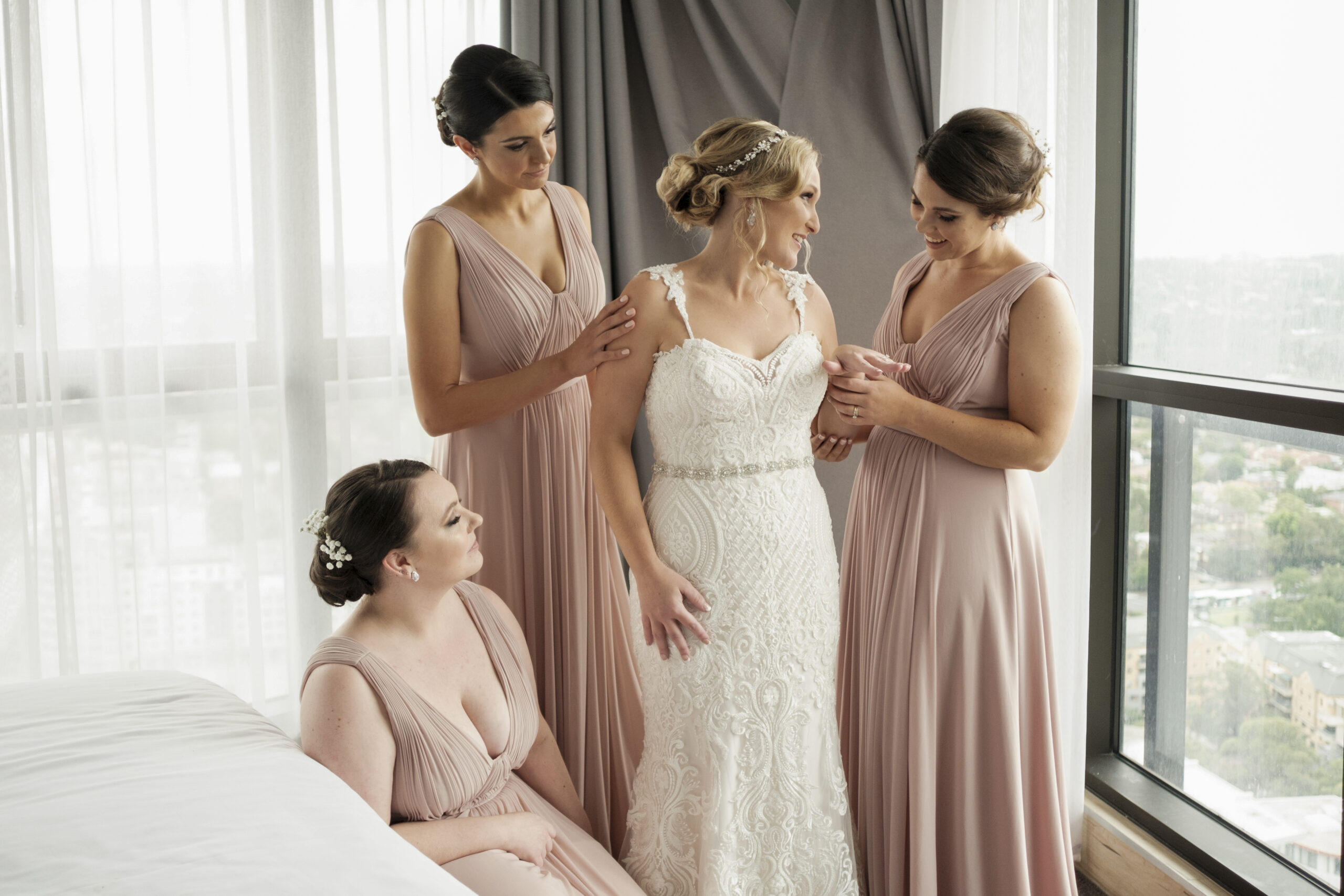 Bride being fitted in to dress with bridesmaids.