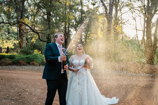 Newly wed couple celebrating wedding in native Australian bushland by popping a bottle of wine and spraying it.